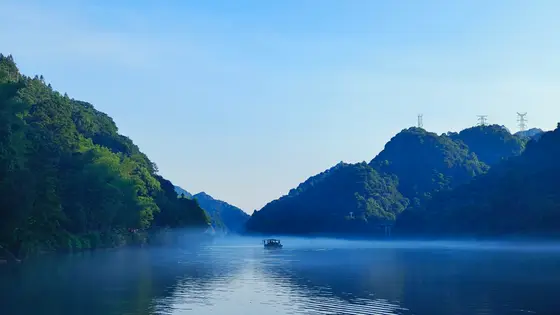 晨光微熹，峡谷间的薄雾似轻纱漫笼水面，晕开一帘朦胧的诗笺。小舟载着清梦悠然驶过，划破水的静谧，漾起细碎的涟漪。两岸青山苍翠如黛，绿意随晨雾轻漾，将天地都浸得温润清新。