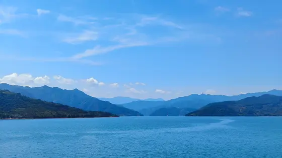 天幕低垂，云朵如絮，远山披着淡淡的青黛，在湖水中勾勒出连绵的倒影。风轻拂过，湖面泛起细碎的涟漪，仿佛大地轻柔的呼吸。一汪碧水静静流淌，将天空的湛蓝与群山的苍翠，都温柔地揽入怀中。此刻，万物静默如谜，唯有这无边的宁静，在天地间缓缓舒展。