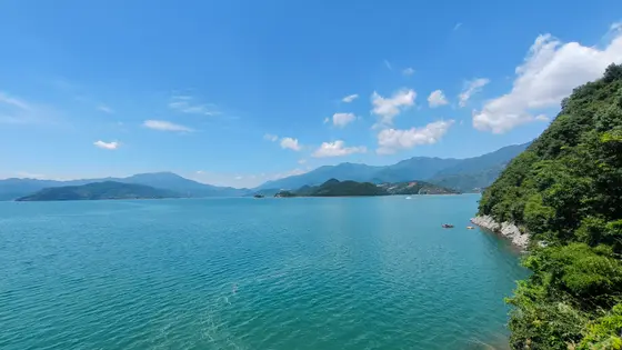 水天一色，碧波轻漾，远山如黛，在云影间起伏绵延。岸边绿意依依，仿佛是山峦温柔的呼吸。一艘小舟静泊于光阴里，载着半湖清风与半湖闲适。