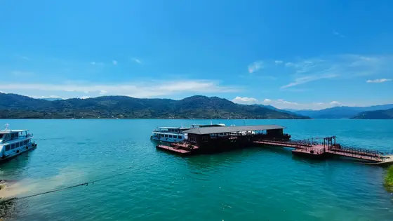 湖水如绸，静静铺展向远山的轮廓，蓝天垂落几笔闲云，便裁出一方澄澈的倒影。红岸泊着几叶轻舟，仿佛时光在此搁浅，只余波光与风声，絮絮说着夏日的私语。