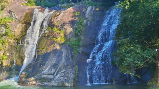 两道白练自青岩间垂落，轻叩深潭，碎玉飞溅成诗。石上朱砂字迹斑驳，与苔痕绿意相映成趣。水流声里，时光仿佛被翠影揉碎，只余清音绕山。