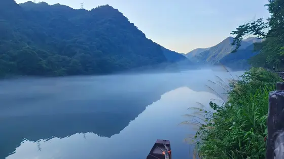 晨雾轻纱笼寒水，青黛山影倒漾成一幅未干的墨痕。一叶孤舟静泊，任涟漪揉碎远山的梦。晨光欲醒未醒，在朦胧里铺开第一笔淡金，万物都在这青蓝调的静谧中，缓缓呼吸。