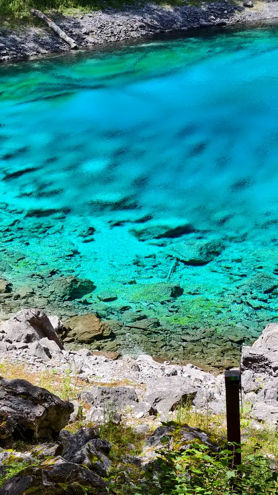 湖水宛如一块流动的翡翠,在阳光下散发着迷人的碧蓝光泽。清澈见底的水面倒映着光影的交织,层层涟漪仿佛在轻声诉说着山间的秘密。岸边的乱石与深邃的湖水相映成趣,构成了一幅静谧而充满生命力的自然画卷。