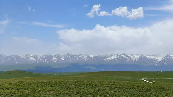 天空如洗，云朵慵懒地卧在山尖。  
雪山静默如亘古的诗篇，草浪轻摇着绿色的呢喃。  
远方的人影缓步其间，成为天地间最温柔的注脚。