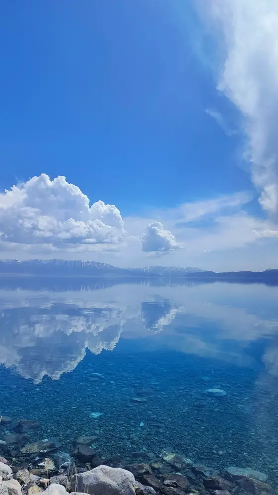湖水轻拥着天空的蓝，云朵在镜中舒展成棉花的形状。  
水底石子如散落的音符，静静诉说深浅的蓝。  
远山戴着雪帽，与倒影相视而笑，时光在此停驻成永恒。