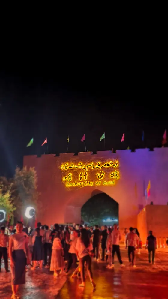 夜色温柔地裹住喀什古城，暖黄与绛紫的光晕在城墙上晕染开。流光织就的拱门下，游人的剪影如时光河流里浮动的星子。风掠过垛口的彩旗，抖落一地异域风情的细语。古巷深处飘来香料与烤馕的暖意，将千年故事揉进了每一盏灯火里。