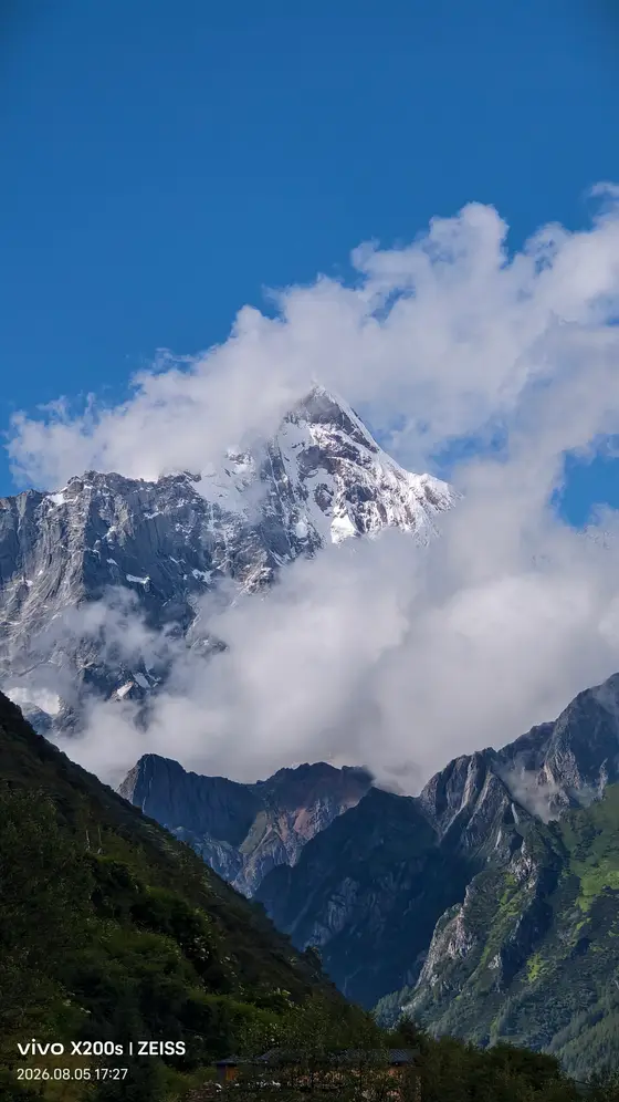 雪峰刺破云霭,在湛蓝的苍穹下勾勒出银白的轮廓。
流云似轻纱缠绕山腰,将巍峨的岩脊化作朦胧的梦境。
近处的苍翠山峦静默伫立,仿佛在仰望一场天地间的无声对话。
阳光为积雪镀上微光,让整片山谷流转着静谧而永恒的呼吸。