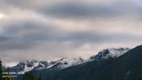 云层低垂,如轻纱般轻抚着沉睡的雪山。
阳光穿透缝隙,为银白的山巅披上流动的金缕。
风在深谷间低语,绿意与积雪在静谧中永恒相依。
此刻,天地只剩一片苍茫的诗意。