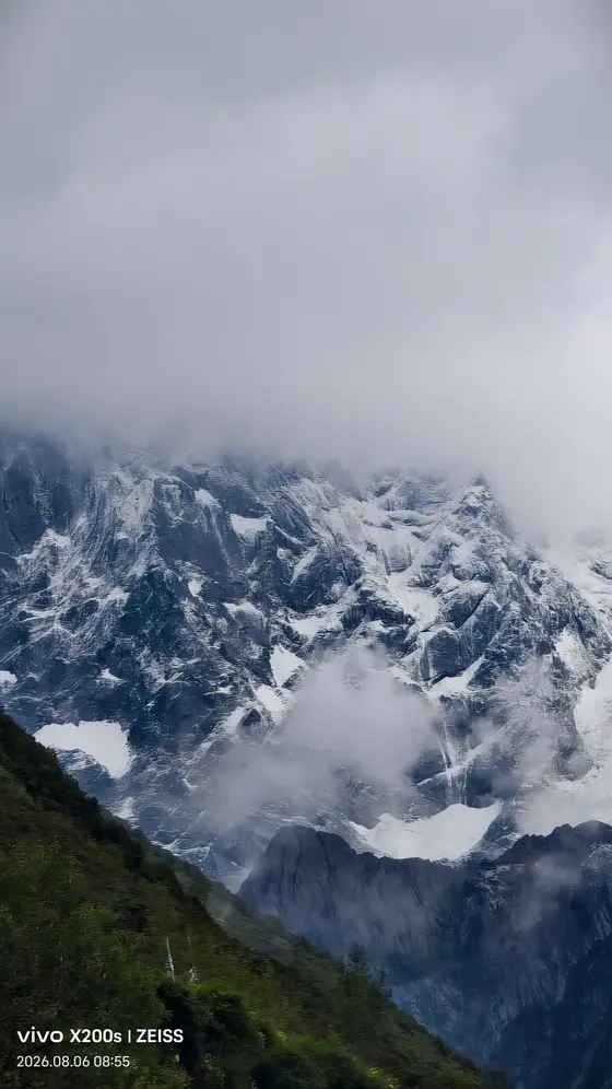 云雾垂落如轻纱,将雪峰半掩于朦胧的呼吸之间。
岩壁的褶皱里藏着冰川的私语,苍绿的山脊托起一片未融化的皎洁。
风在此处凝成白色的絮语,每一缕雾气都缠绕着亘古的寂静。
而沉默的雪山,只是垂眸凝视着人间升起的尘烟。