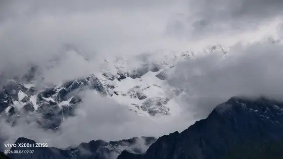 云雾轻纱缓缓揭开天际的帷幕,雪山峰尖如利剑刺破苍茫。万年积雪在灰白的天幕下沉默不语,唯有风在冰川的褶皱间低吟。近处的黛色山峦仰望着那片圣洁的白,仿佛尘世与仙境之间,只隔着一层流动的雾。