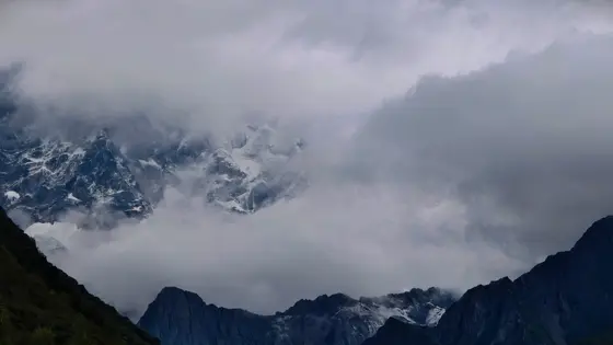 云雾轻纱半遮面,雪山尖峰若隐若现,仿佛是天界遗落人间的一幅水墨丹青。灰蓝色的苍穹之下,层峦叠嶂在迷蒙中沉睡,唯有那冰川的微光,如时间的碎屑,在静谧中闪烁。这一刻,山与云的缠绵,便是大地写给天空最深沉的情诗。