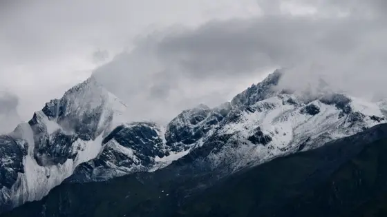 雪峰披着银甲,静静刺入云层深处,仿佛与天空低语。云雾如轻纱缓缓漫过山脊,时而隐去岩棱的锋芒,时而显露出冰川冷冽的光泽。时间在这里凝成一片苍茫,唯有风的呼吸在冰川的褶皱间流转,低吟着亘古的寂静。