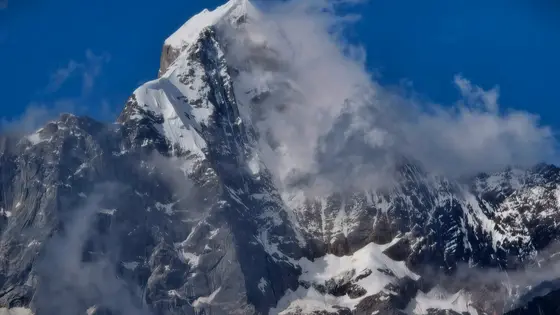 雪峰如利剑刺破云霄,万载冰晶在日光下闪烁着冷寂的光晕。流云似轻纱缠绕山腰,将巍峨的轮廓时而隐入朦胧,时而托举向湛蓝的苍穹。深黑的岩壁上镌刻着岁月剥蚀的痕迹,每一道裂隙都诉说着亘古的沉默。