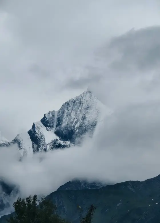 云雾轻挽着雪山的腰际,峰尖破开苍茫的灰白,如一柄刺向天穹的银剑。白雪覆于万仞之巅,似神明遗落人间的冠冕,在云海沉浮间若隐若现。风过无痕,唯留一山寂寥与亘古的沉默。