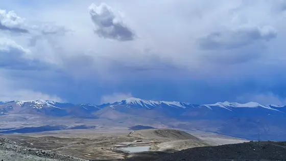 云层低垂如沉睡的巨兽，将雪山染成水墨长卷。银顶峰峦是天地间沉默的王冠，俯瞰着荒原与蜿蜒的小径。风掠过时，连影子都泛起古老而温柔的蓝色。
