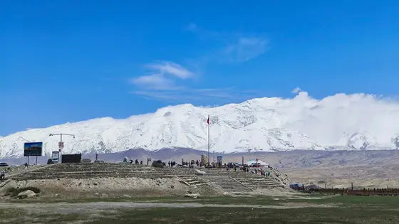 神山静卧于天际，皑皑白雪与流云相拥，仿佛为大地披上了圣洁的哈达。石阶上人群如星点，仰望着这份亘古的庄严。风拂过荒原，带来雪山深处的低语，诉说着自然与岁月的永恒诗篇。