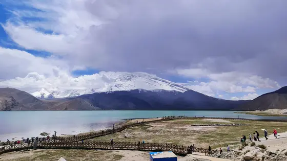 蓝天白云轻抚雪山巅，冰晶闪耀似银练垂天。湖水澄澈如玉镜，倒映着山的轮廓，云的缠绵。栈道蜿蜒通向湖心，游人如织，漫步在这天地之间。风轻拂过，带着雪的清凉，云的温柔，让人心醉神迷。