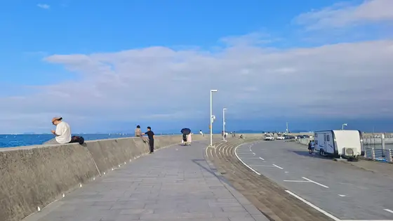 天穹低垂，云絮慵懒地铺展成海的呼吸。  
堤岸延伸向湛蓝的尽头，浪涛在远处轻声絮语。  
行人如时间的微尘，在光与影的缝隙间缓慢移动。  
唯有那辆白色旅居车，像停泊在时光岸边的贝壳，守护着海风里散落的遐想。