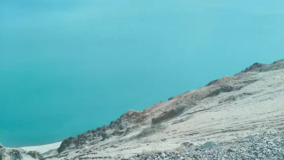 静谧的蓝绿色水面缓缓倾泻，浅灰色的山崖如岁月的脊梁斜倚水畔。阳光为山石镀上暖意，水波细碎地折射着天光，天地在此刻凝成一幅清寂的水墨。