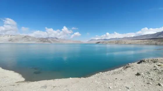 湖水如一块巨大的蓝宝石，倒映着无瑕的天空。远方的山峦连绵起伏，仿佛大地的脊梁，沉静地守护着这片碧波。云朵悠悠飘过，在水面上留下轻轻的痕迹。