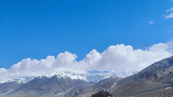 天幕蓝得如洗，云朵却轻拥着雪峰。山脊线在光影里起伏，仿佛巨龙蜿蜒的脊背。那一片皎白之下，藏着亘古的寂静，而人间烟火，就在这壮阔的呼吸之间。