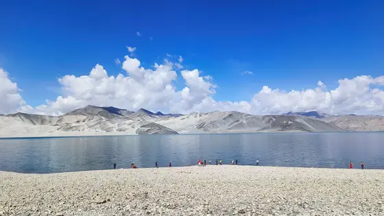 天光倾泻，将万里云絮揉碎成雪山的圣洁衣襟。湖水低语，倒映着亿万年时光的剔透。砾石滩上，渺小的身影与天地对望。