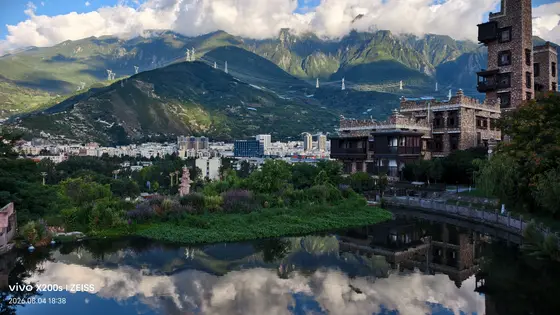 一池静水轻抚着山影，古堡的棱角在镜中软成岁月的笔触。雪峰披着云裳低语，将天空的蓝与山峦的绿绣成大地的衣袂。远处的城郭如散落的棋子，静卧在时光的褶皱里，而近处的草木正捧着露珠，把晨昏酿成一盏未饮的茶。
