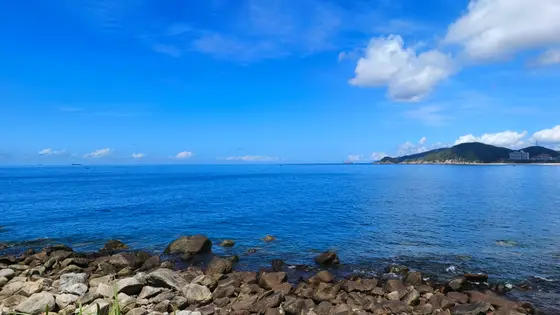 海浪轻抚着岸边的礁石，仿佛在低语着古老的歌谣。蓝天如洗，白云悠然飘过，将远方的岛屿勾勒成一幅淡雅的剪影。波光粼粼的海面，映照着时光的流转，让每一步靠近海岸的脚步，都变得轻柔而宁静。